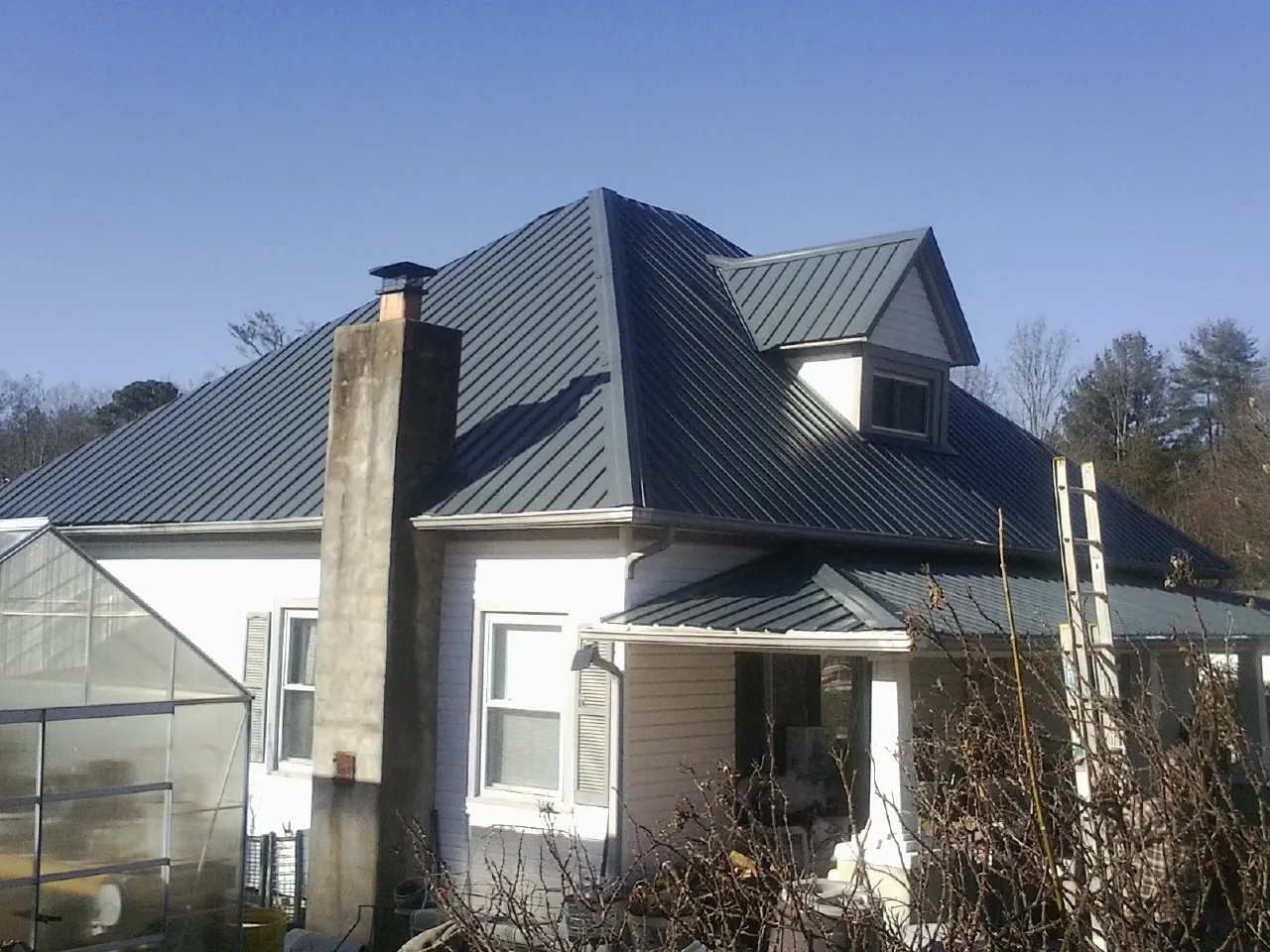 Dark blue standing seam metal roof on a white farmhouse with dormer — Slate & Tile Roof Repair by Roofing Brothers in New Iberia
