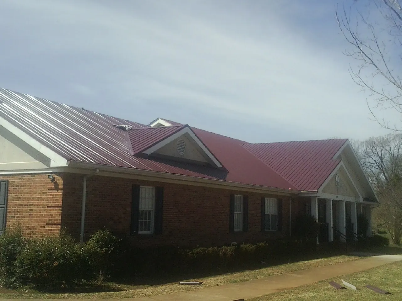 Red metal roof with gabled entries on a long brick building, from a Hail Damage Roof Repair job in New Iberia