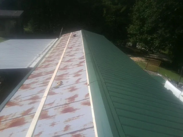 Old rusted panels beside newly installed green metal roofing — Wind Damage Roof Repair by Roofing Brothers in New Iberia