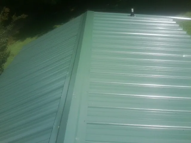 New green metal panels meeting at the ridge of a roof — Flat Roof Repair work by our crew in New Iberia