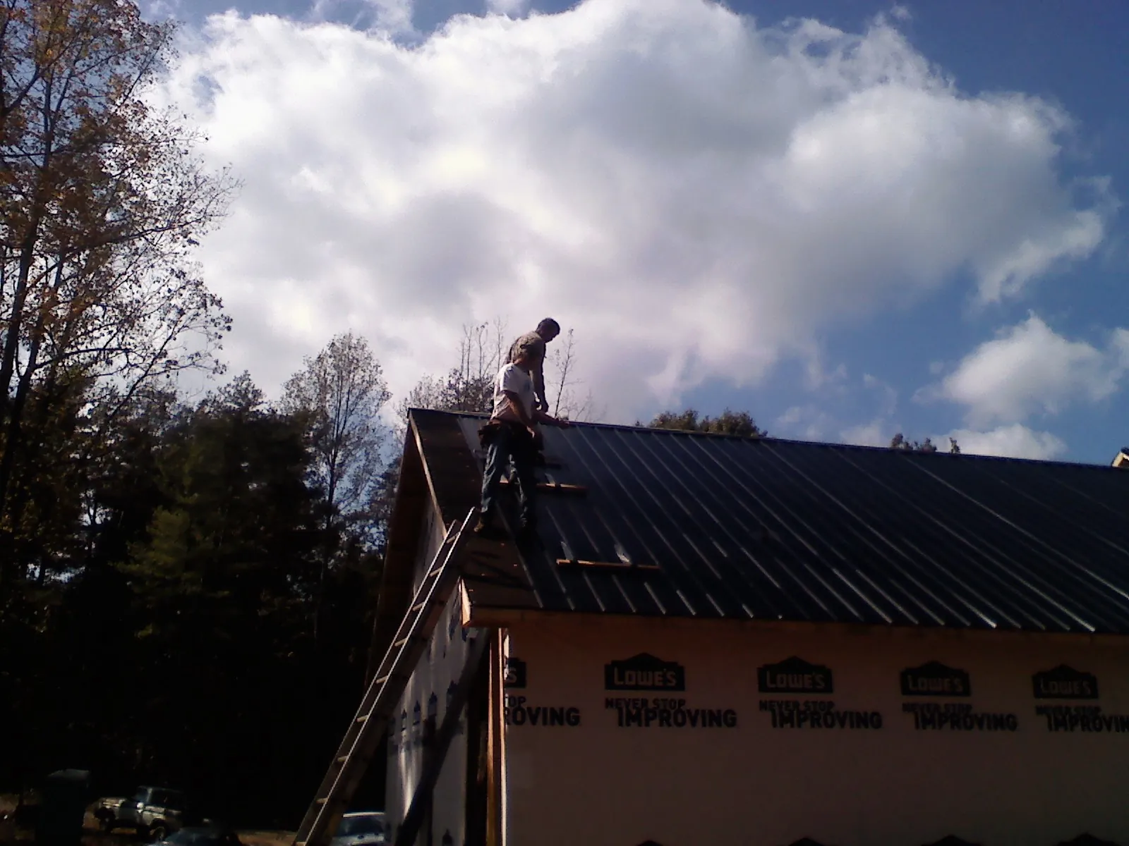 Roofer fastening dark metal panels high against a cloudy sky, from a Roof Inspection job in New Iberia