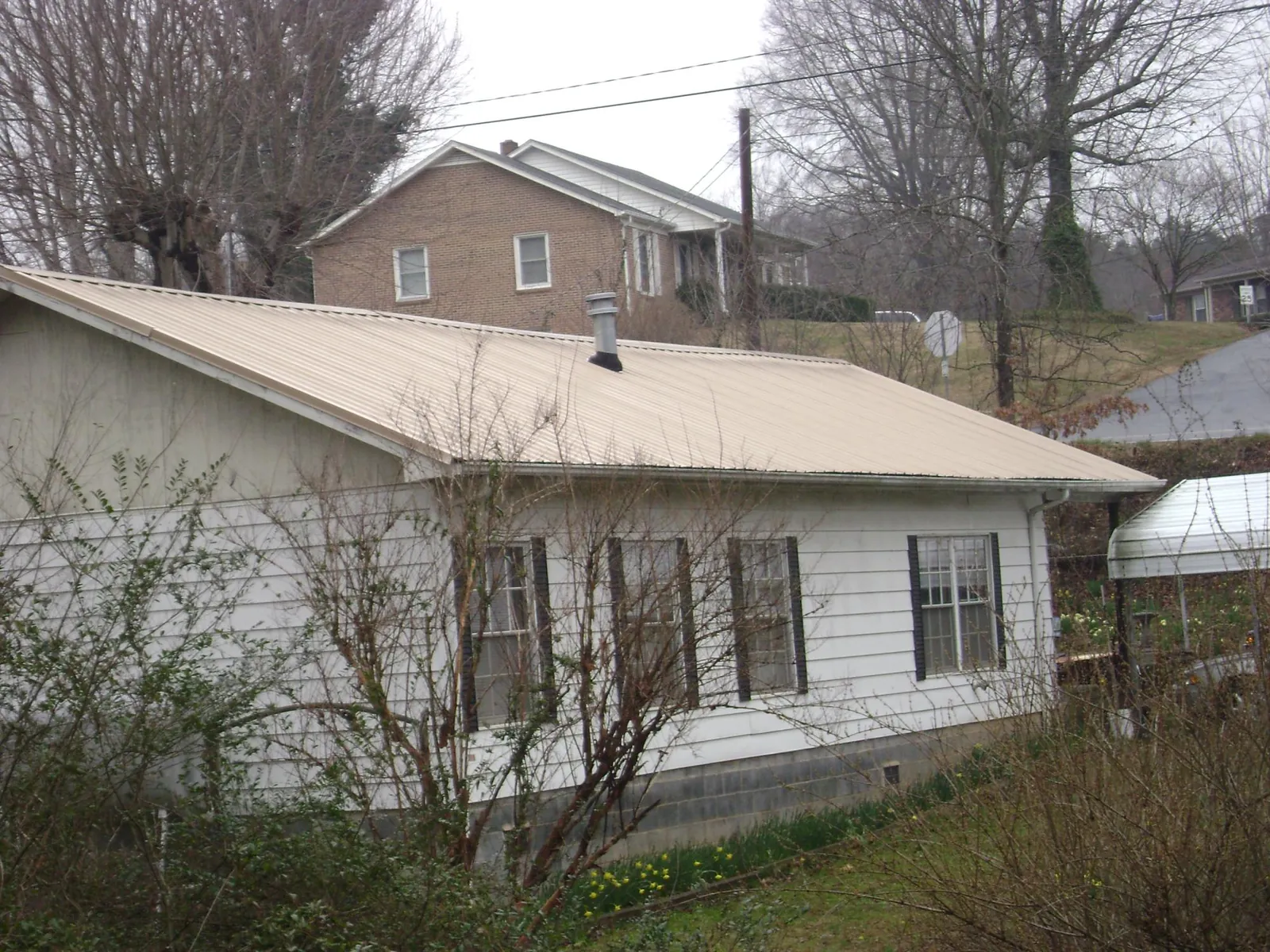 Tan metal roof on a white sided house set into a hillside — Commercial Roofing by Roofing Brothers in New Iberia