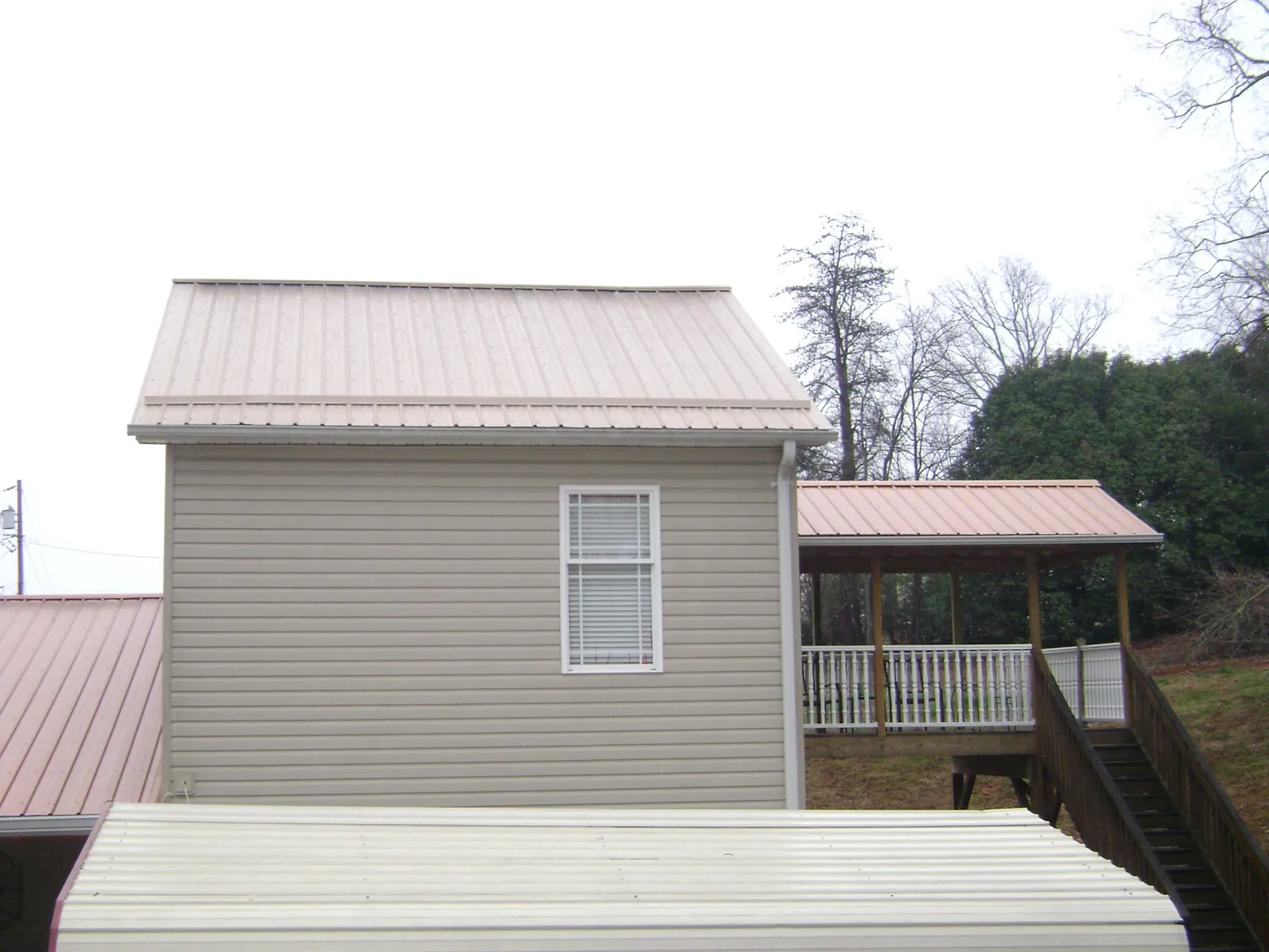 Tan metal roofs on a two story addition and attached porch, from a Roof Replacement job in New Iberia